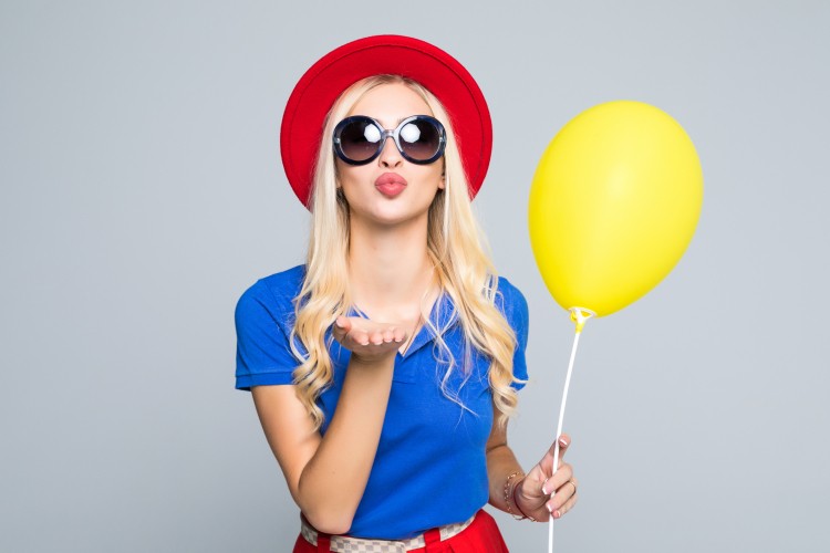 Pretty-young-woman-in-sunglasses-with-air-balloon-sends-an-air-kiss-over-gray-background-845194082_2