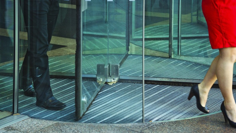 Busnessman-And-Businesswoman-Walking-Through-Revolving-Door-482802851_1800x1200.jpeg